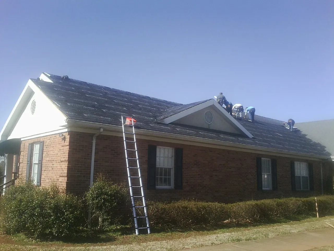 Crew tearing shingles off a brick ranch roof with a ladder set — Emergency Roof Repair work by our crew in Cave Junction