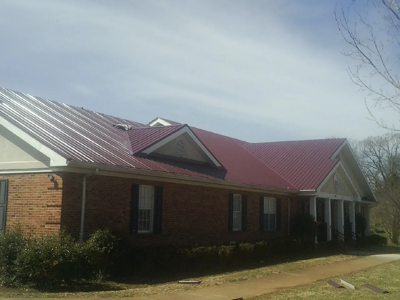 Red metal roof with gabled entries on a long brick building, from a Hail Damage Roof Repair job in Cave Junction