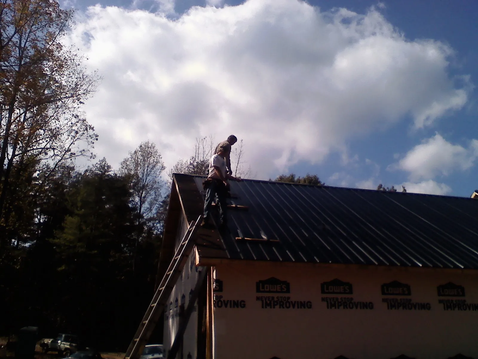 Roofer fastening dark metal panels high against a cloudy sky, from a Roof Inspection job in Cave Junction
