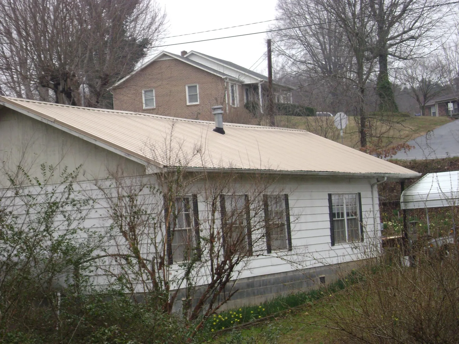 Tan metal roof on a white sided house set into a hillside — Commercial Roofing by Roofing Brothers in Cave Junction